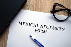 A photo of a medical necessity form with a pen and glasses laying on the top